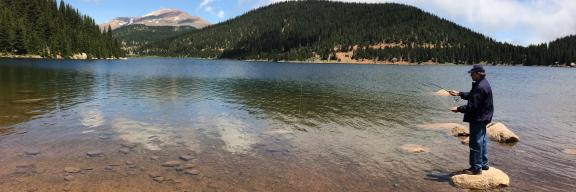 man fishing in large reservoir with pike peak in the background