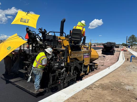 A construction crew rides on a paving vehicle as they pave the east side of Black Forest Road.