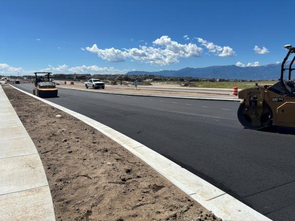 A view of the east side of Black Forest Road with freshly paved asphalt. Construction vehicles are visible on the road.