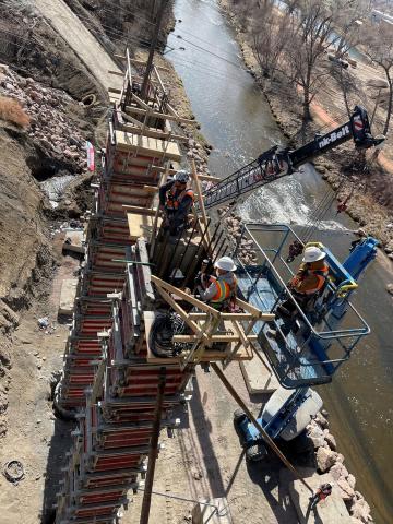 Heavy machinery is lifting tall bridge supports into place against a blue sky