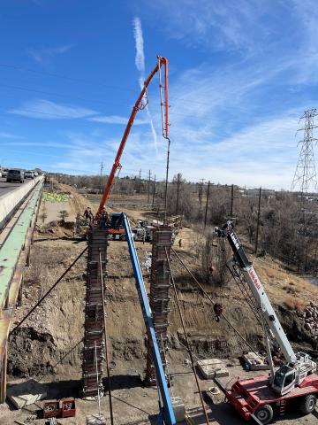 Heavy machinery is lifting tall bridge supports into place against a blue sky