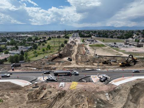 A west-looking view of the intersection of Barnes Rd. and Marksheffel Rd. in August 2024. The intersection is mostly dirt as work is done to pave it, vehicles and traffic hazard equipment are all around.