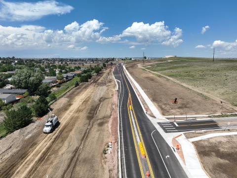 Northbound view of Marksheffel Rd. at Graphite Rd. in August 2024. The road is freshly paved, with dirt on the left side.