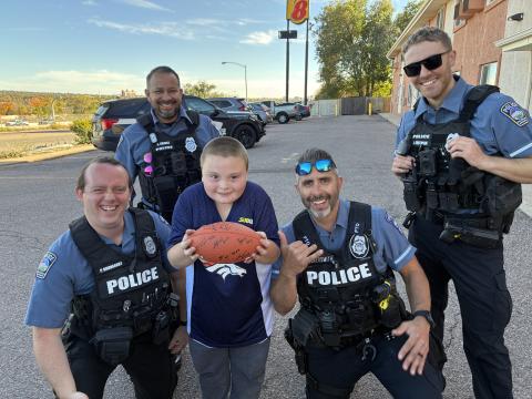 A group of four officers and Mackenzie in the middle of them. Mackenzie is holding the football and they are all posing for a picture together. 