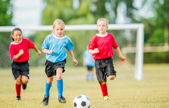 a little girl dribbles a soccer ball as two other kids on the opposite team try to catch her