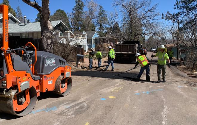 three people patching a section of pavement across the width of the road