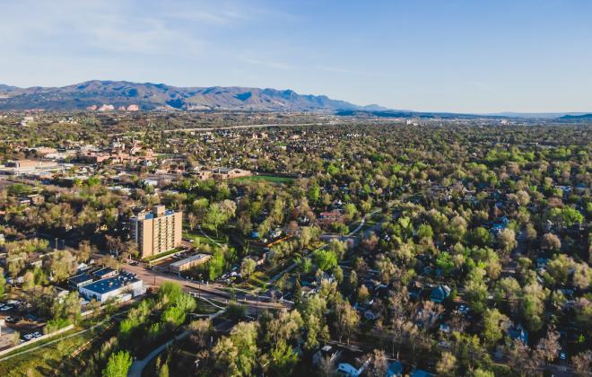 aerial view of trees across Colorado Springs with mountains in the background.