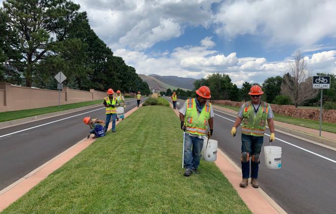 workers in yellow safety jackets clean up trash from a grassy median