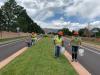 workers in yellow safety jackets clean up trash from a grassy median